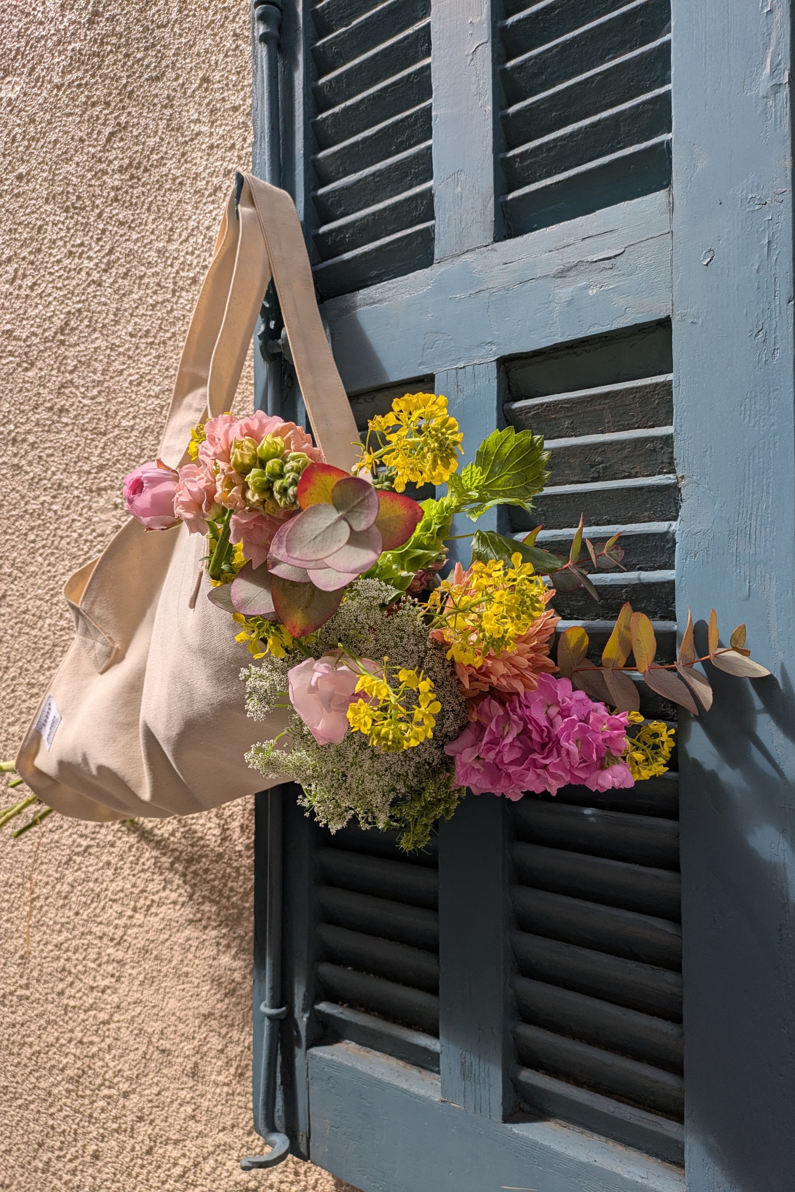 Floral arrangement attached to a door with a beige tote-bag.