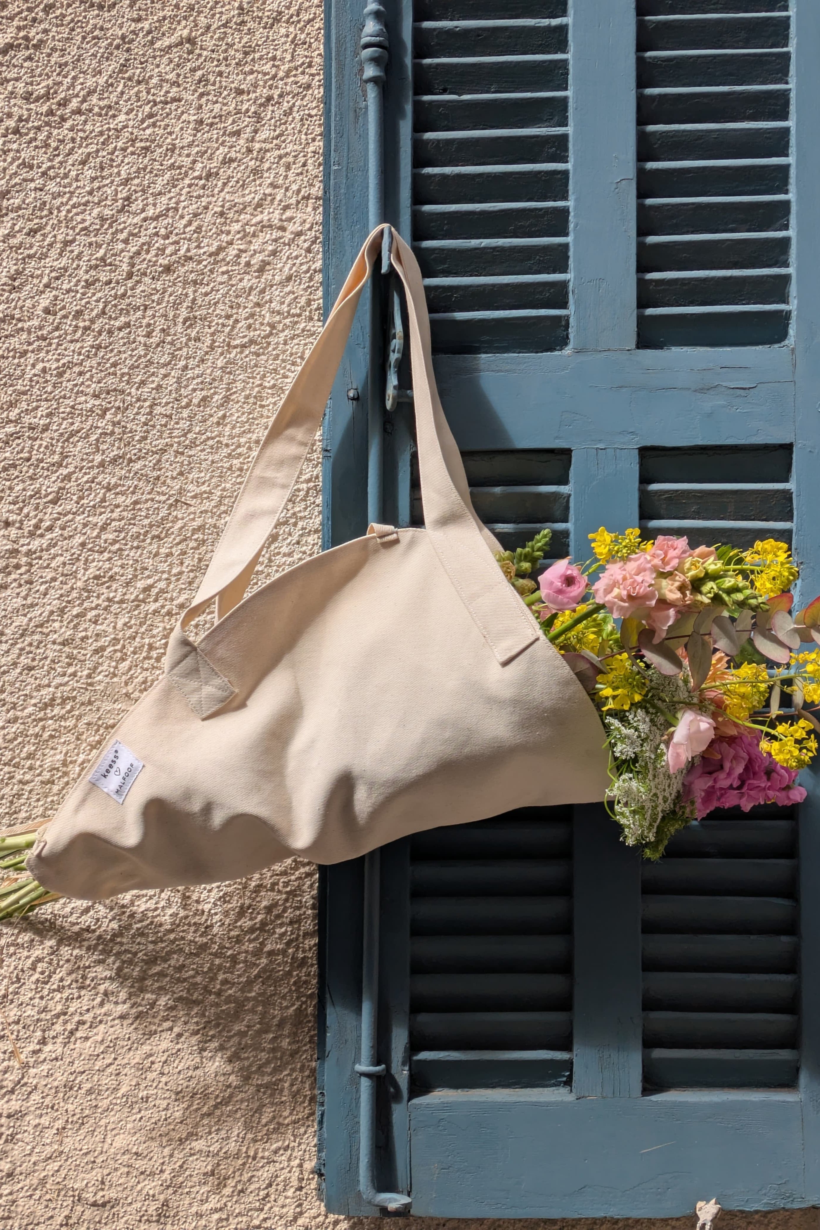 Beige tote bag with flowers against a textured wall and blue shutter.